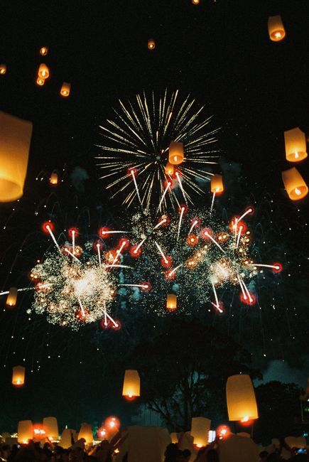 The image depicts a nighttime outdoor celebration with numerous sky lanterns ascending into the dark sky, illuminated by fireworks displaying bursts of white, red, and gold sparks. The lanterns, made of paper with small flames at their bases, float amidst the fireworks, creating a vibrant and festive atmosphere. Below, silhouettes of gathered people can be seen watching the display, with a dark tree line visible in the background. The scene captures a moment of collective celebration, with the lanterns and fireworks filling the sky with light. This setting relates to a festive event, and while the image is not directly related to house removals or moving services, the context of large gatherings and outdoor celebrations can be associated with community events or celebrations before or after a home relocation. Man with Van Penge offers professional removals services that support smooth packing, transportation, and delivery during house moves, ensuring a reliable process for clients in the SE20 area during occasions that may involve festivities or large-scale planning.